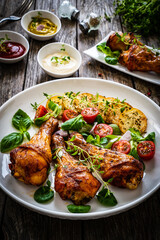 Barbecue chicken drumsticks with fried potato, lettuce and mini tomatoes on wooden table

