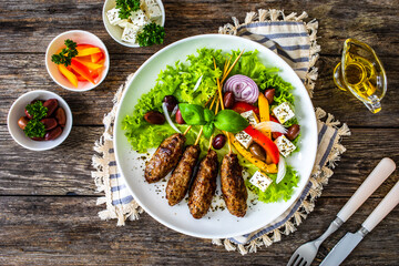 Souvlaki - greek shashlik served with fresh green vegetables and feta cheese on wooden table
