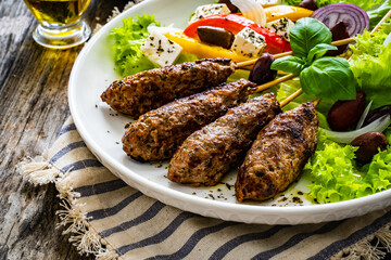 Souvlaki - greek shashlik served with fresh green vegetables and feta cheese on wooden table
