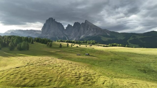 Amazing view on Dolomites peak with a hiking path leading to the mountains. Sunrise drone shot of idyllic Alpe di Suisi mountains in South Tyrol. Wooden cottages at sunrise.