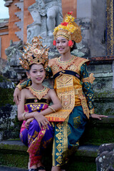 Fototapeta na wymiar Two young Bali smiling girls make -up dressed in traditional colored costumes inside in the temple.