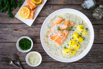 Roasted trout fillet with potatoes and dill sauce served on wooden table
