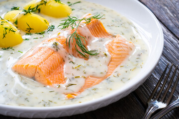 Roasted trout fillet with potatoes and dill sauce served on wooden table
