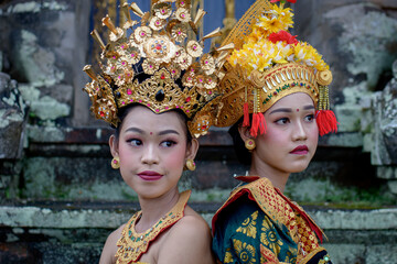 Two young Bali smiling girls make -up dressed in traditional colored costumes inside in the temple.