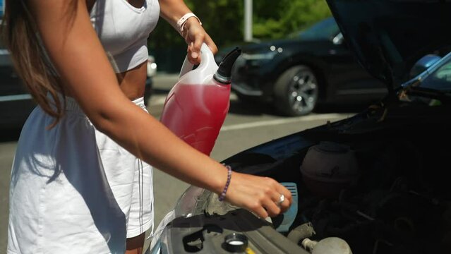 Young woman pouring antifreeze car screen wash liquid into car