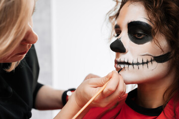 A makeup artist makes up a demon to a young girl in a beauty salon. Halloween Celebration Concept