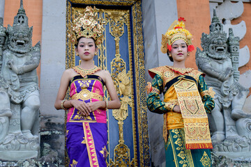 Obraz premium Two young Bali smiling girls make -up dressed in traditional colored costumes inside in the temple.