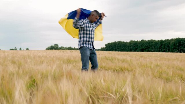 Agronomist in the middle of the field with the flag of Ukraine on his shoulders.