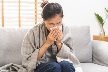Sick, Coronavirus covid-19 asian young woman, girl headache under blanket have a fever, flu and use tissues paper sneezing nose, runny sitting on sofa bed at home. Health care on virus person.