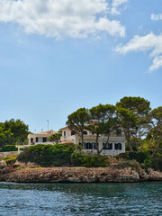 Fototapeta na wymiar Villa by the sea behind the trees on the rocky coast, Ciutadella, Menorca, Spain