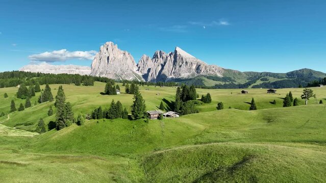 Amazing view on Dolomites peak with a hiking path leading to the mountains. Sunrise drone shot of idyllic Alpe di Suisi mountains in South Tyrol. Wooden cottages at sunrise.