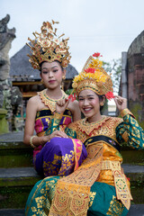 Two young Bali smiling girls make -up dressed in traditional colored costumes inside in the temple.