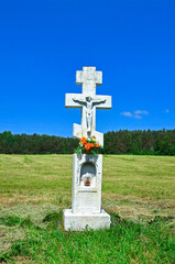 Fototapeta na wymiar White stone cross on spring time scenery, Low Beskids, Poland. This region are a mountain range with wide open spaces, wildlife, deserted villages and stone crosses by the roadside