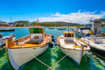 Fototapeta premium Beautiful view of Greek fishing boats anchored in a small village. Whitewashed houses, fishing boat, clear blue sky, bay, sea, hills. Milos, Greece