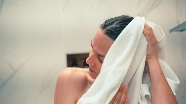 Close-up shot of a young woman wiping her face and hair with a white towel after a shower