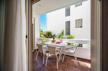 Fototapeta na wymiar Balcony with furniture, white table served with fruits and wine glasses, four chairs, sunny summer day, holiday concept. 