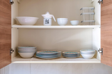 Opened cupboard with kitchenware inside. Kitchen details.