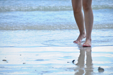 Two legs of lady walking forward on sandy wet beach of the sea with reflection
