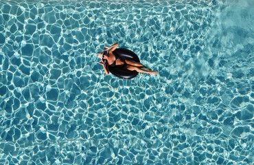 smiling woman in black bikini and hat floating on swimming pool water