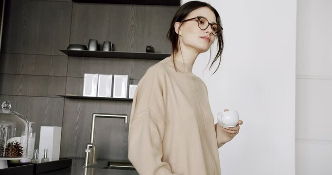 A beautiful Young woman is drinking coffee and tea in the modern kitchen room at home, healthy calm lady relaxing on minimalist dining room. feel stress free at home lounge alone. Woman rests at home.