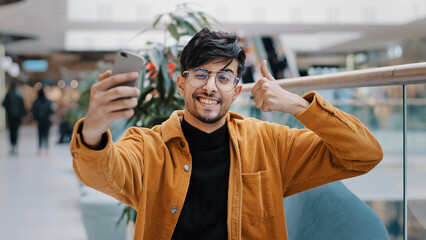 Young handsome arab guy blogger model holding phone in hand photographed on mobile camera posing smiling making gesture taking photo filming video for blog on smartphone using video chat application