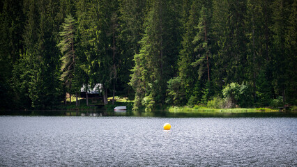 Idylle am See, eine gelbe Boje schwimmt auf dem Wasser, am Ufer liegt ein Ruderboot neben einer...