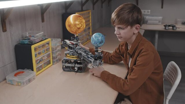 High angle shot of modern Caucasian boy sitting at table creating robotic solar system model for school project