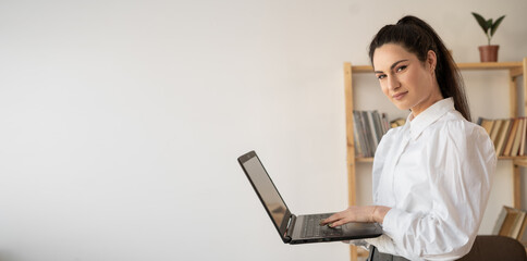 Successful hispanic millennial woman using and typing on laptop in modern office looking at camera. Female in business concept.