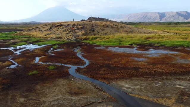 An incredible drone shot of the stunning landscape of Lake Natron with people standing on a hill top with Ol Doinyo Lengai volcano in the background in Tanzania in North Africa