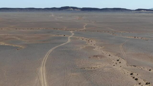 Tire marks on desert landscape in Errachidia region of Morocco near Gara Medouar rock formation. Aerial birds eye pov