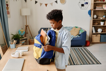 Child preparing his school bag for school packing books and copybooks in it
