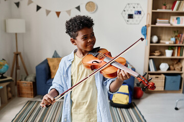 African boy playing violin during lesson while standing in his room at home
