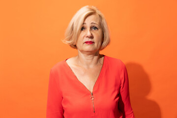 Sad charming middle age woman with blond hair posing isolated on orange color background. Concept...