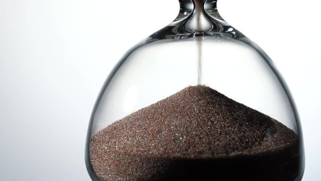 Hourglass placed on white background. Close-up of sand.
