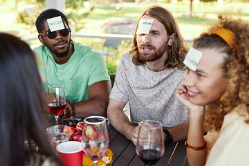 Fototapeta Young man with sticker note on head playing Guess who game with diverse group of friends at outdoor party obraz
