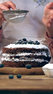 vertical video of cropped woman sifting sugar powder on creamy cake