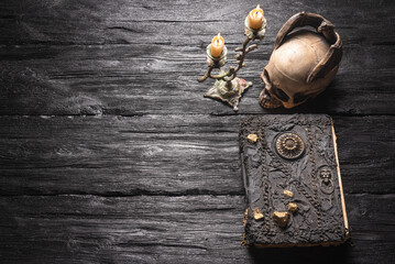 Magic book, skull and burning candle on the old wooden table background.