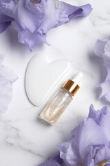 Serum with floral extracts for skincare, Gua sha stone for face massage. Nature cosmetics in glass bottle with pipette and iris flowers. Face and body care spa concept.