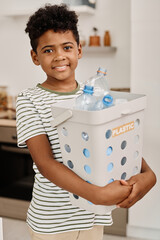Portrait of African little boy smiling at camera holding container with plastic bottles for...