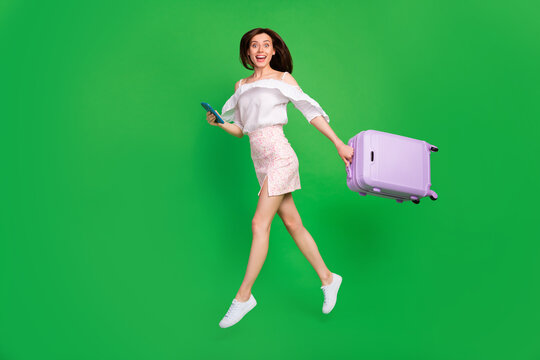 Full length profile photo of attractive energetic person hold suitcase jumping isolated on green color background