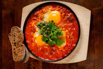 ..Shakshuka with eggs, tomato, and parsley in a cast iron pan.