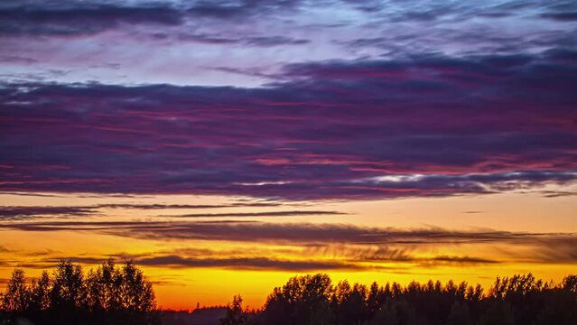 A colorful layered sunset cloudscape over a forest - time lapse