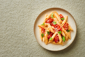 Freshly made penne pasta with cherry tomatoes, basil and parmesan cheese top view with copy space