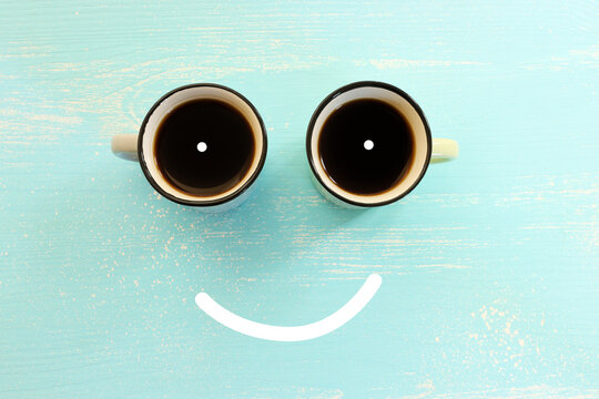 Top view image of coffee cups and smiling face over blue wooden table. Happiness and joy concept