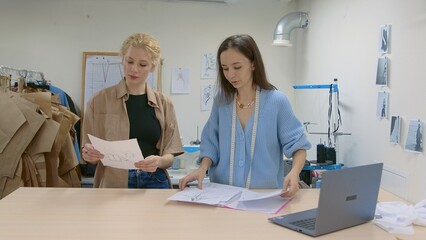 4K. A young female seamstress works with a client in a sewing workshop. They are looking at sketches of dresses