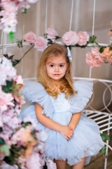 Obraz na płótnie Canvas portrait of a cute little blonde fashion girl in a blue beautiful dress in a vintage interior, decoration with flowers, looking at the camera, space for text
