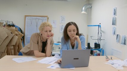 4K. A young female seamstress works with a client in a sewing workshop. They are looking at sketches of dresses