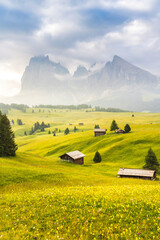 Ethereal green landscape with view of huts and trees on rolling hills and mountains hidden in fog at Sunrise of Alp De Suisi, Dolomites, Italy - 522233282
