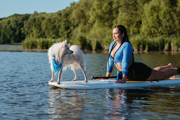 Woman Doing Stretching While Paddleboarding with Her Pet on the City Lake, Snowy Japanese Spitz Dog Standing on Sup Board