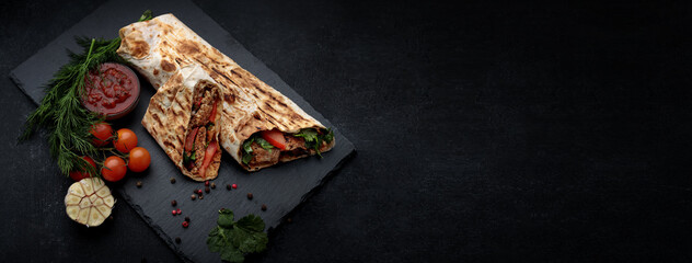 Shawarma with meat, cutaway, with sauce, tomatoes, cheese, herbs and garlic, on black slate, on a...